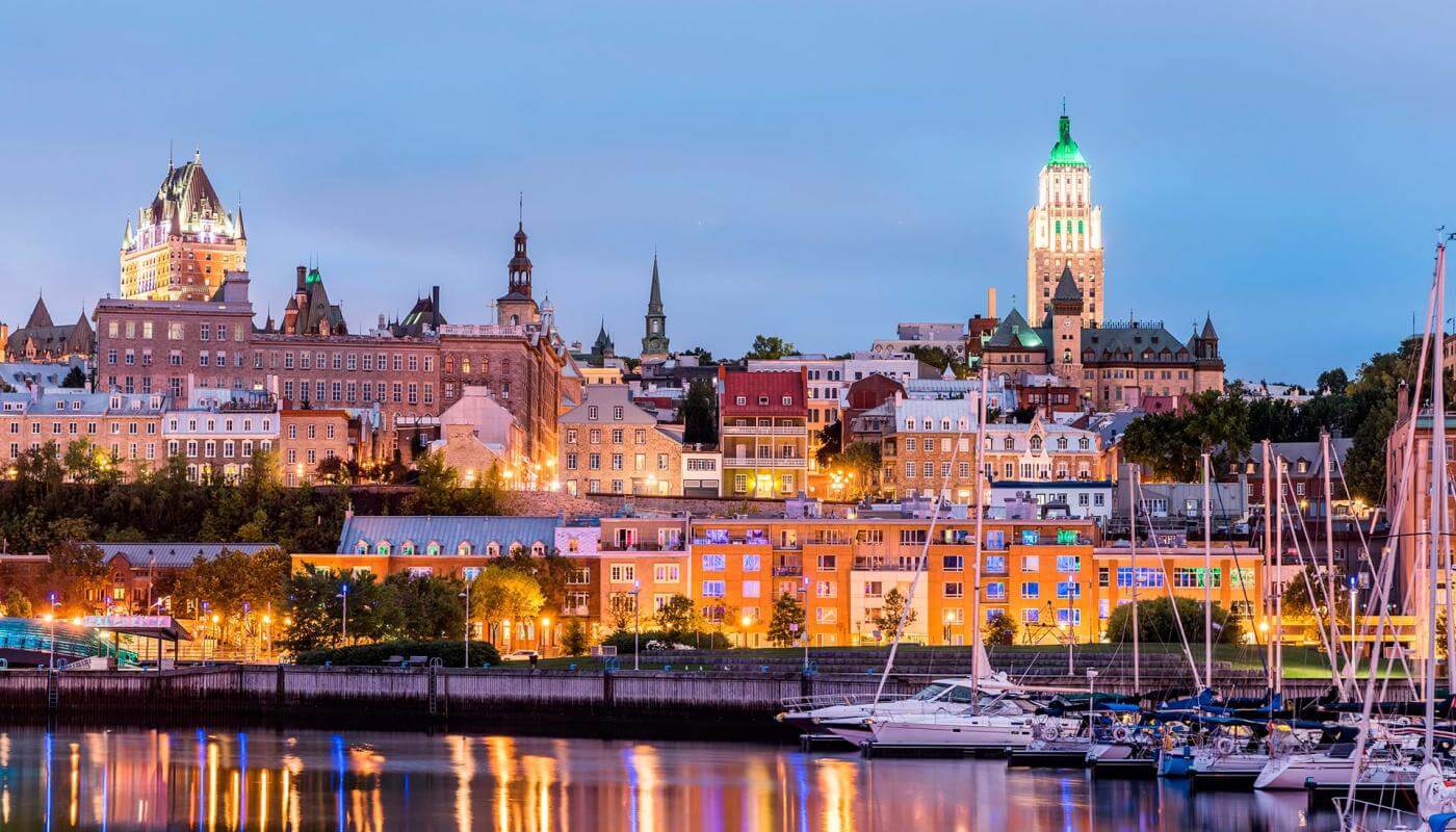 From the Louise Basin, view of the illuminated Old Port, the sailboats, the Château Frontenac and the Price building, in the evening.