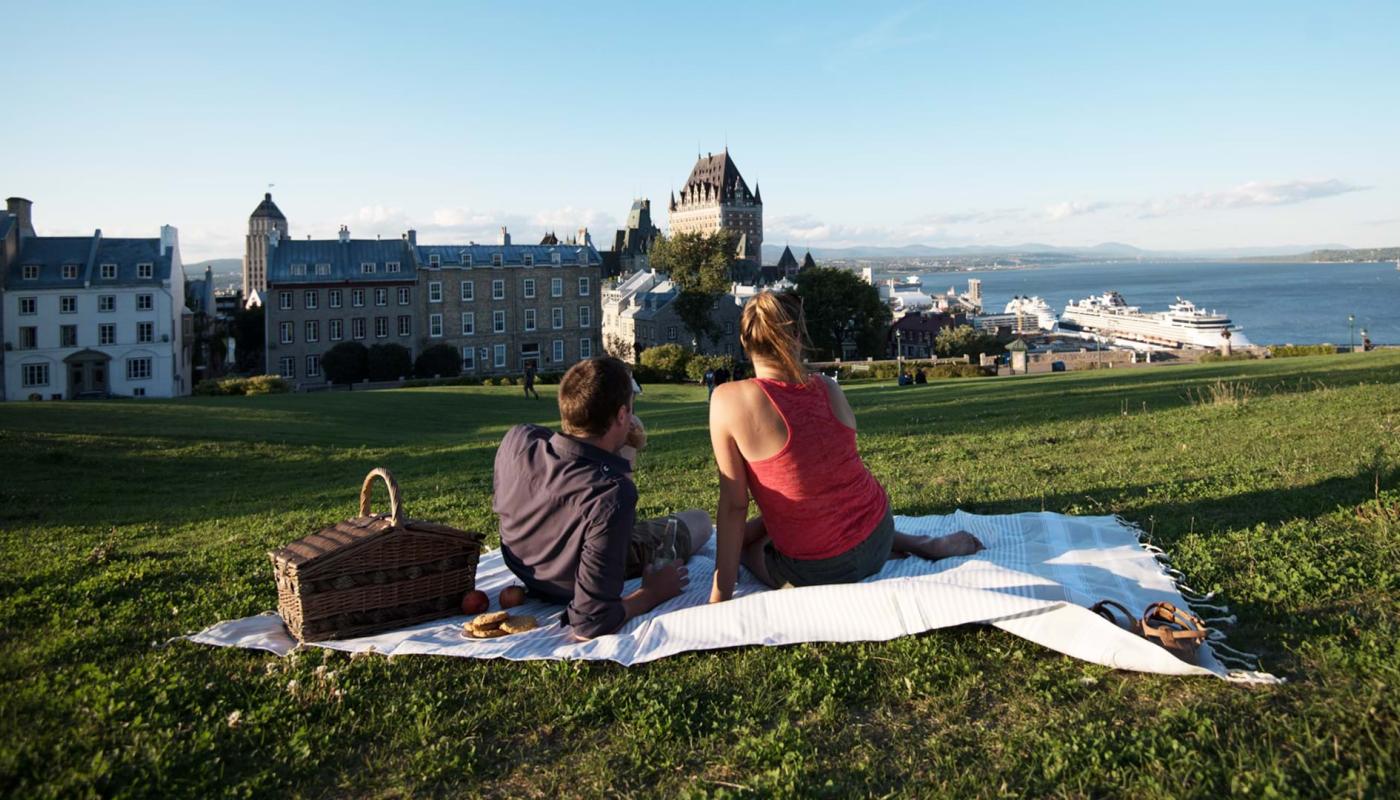 Couple picnicking near the Pierre-Dugua-De Mons terrace while admiring the Château Frontenac and the St. Lawrence River.