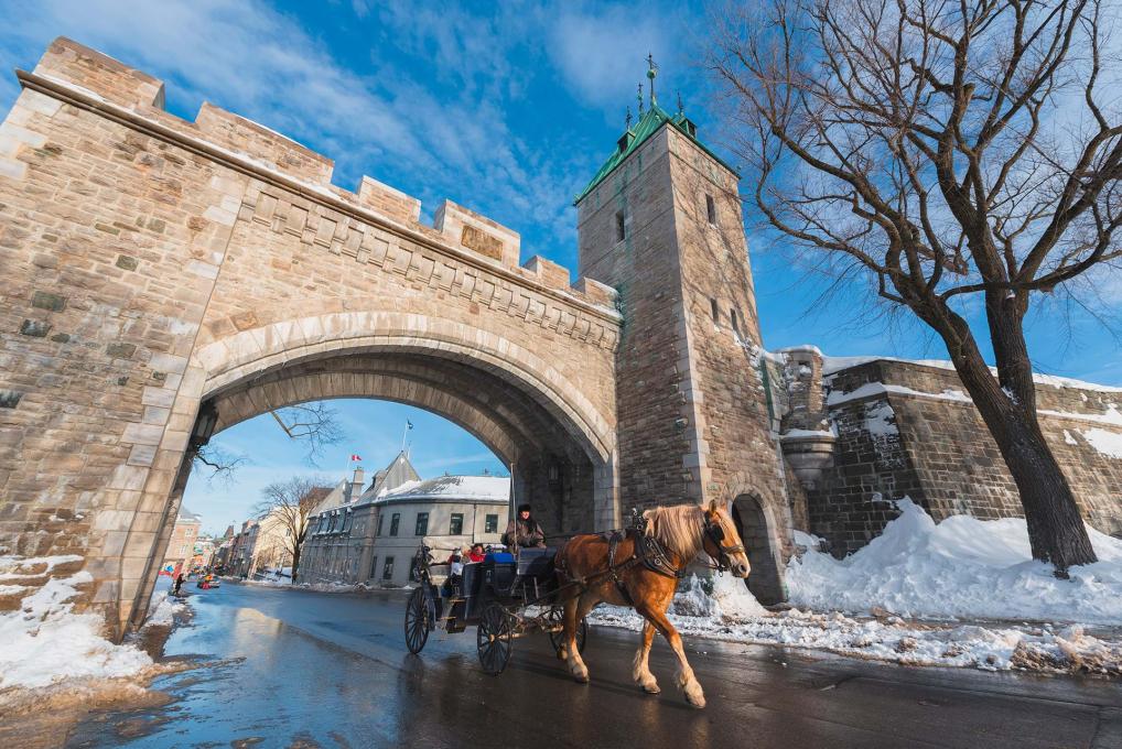 Deux touristes en calèche passent sous la porte Saint-Louis en hiver.