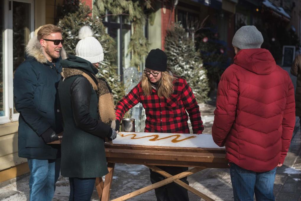 Three people stop in the Petit-Champlain district to taste taffy on snow in a small sugar shack.