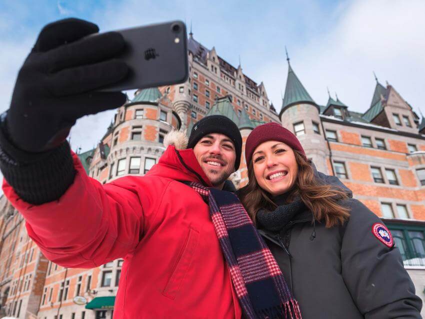 Um casal sorridente tira uma foto sua em frente ao Château Frontenac, no inverno.