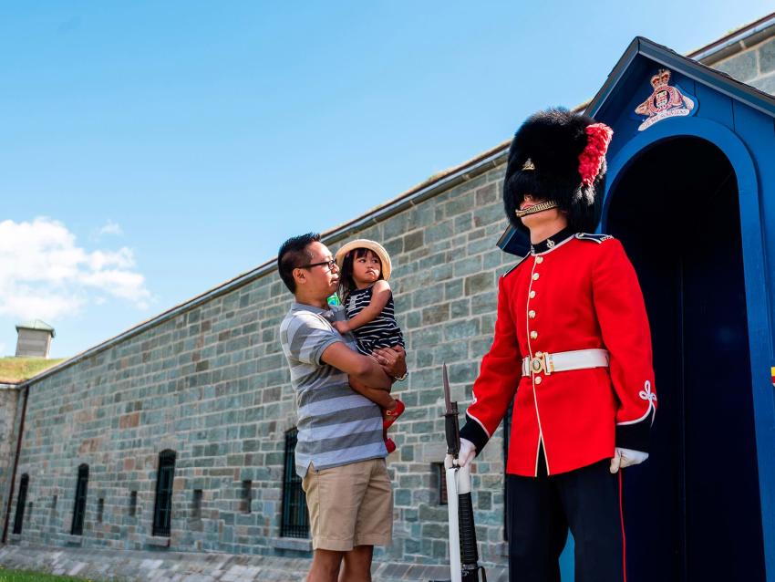 Um pai e sua filha assistem a um guarda vestido com uniformes tradicionais em frente à porta da frente do Citadelle de Québec.